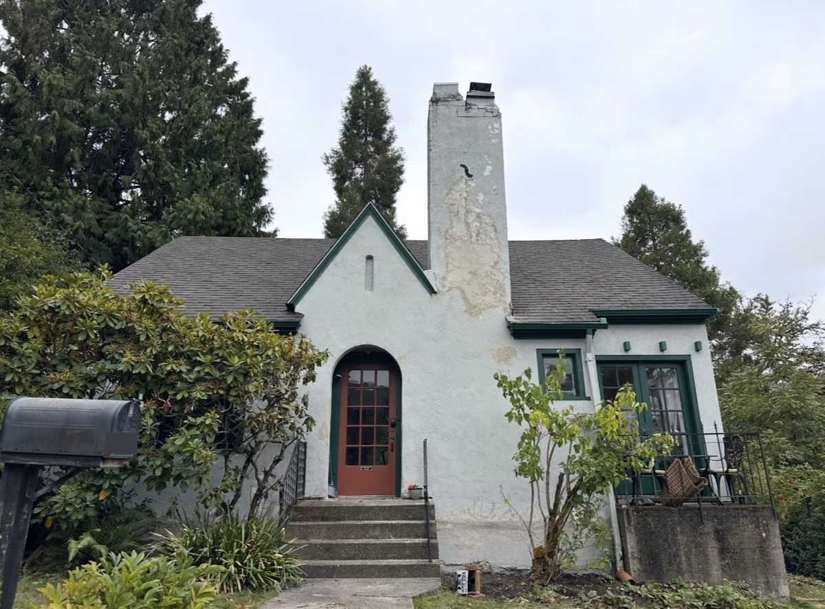 The same cottage before painting, with peeling stucco and green trim