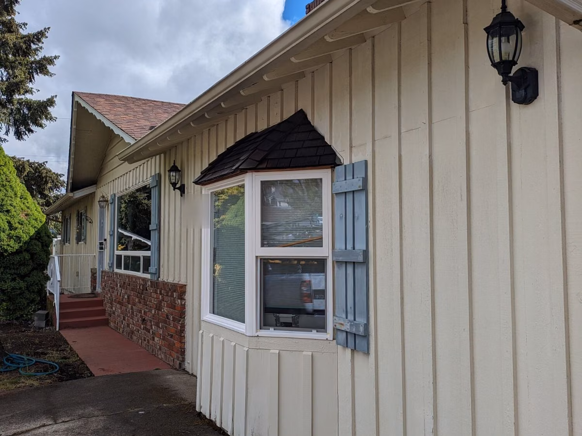 Front of a ranch home before painting, with blue-gray shutters